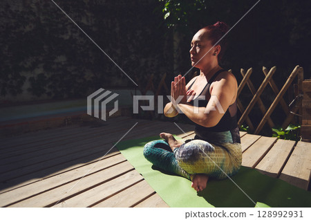 Woman Practicing Yoga Outdoors in Meditative Pose on Wooden Deck Woman Practicing Yoga Outdoors in Meditative Pose on Wooden Deck 128992931