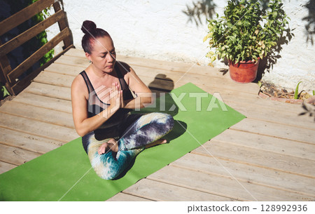 Woman Practicing Yoga Outdoors in a Peaceful Garden Setting on a Green Mat Woman Practicing Yoga Outdoors in a Peaceful Garden Setting on a Green Mat 128992936