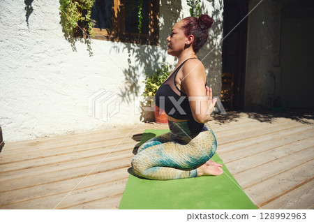 Woman Practicing Yoga Outdoors on a Sunny Day on a Wooden Deck 128992963