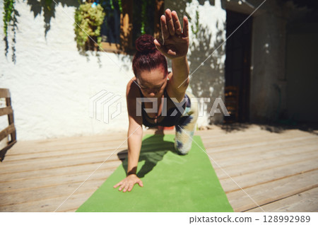 Woman Practicing Yoga Outdoors on a Wooden Deck Under Natural Sunlight 128992989