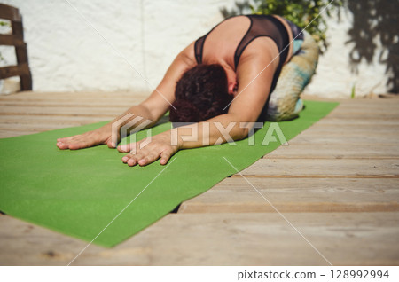 Woman Practicing Child's Pose Yoga Outdoors on a Sunny Deck 128992994
