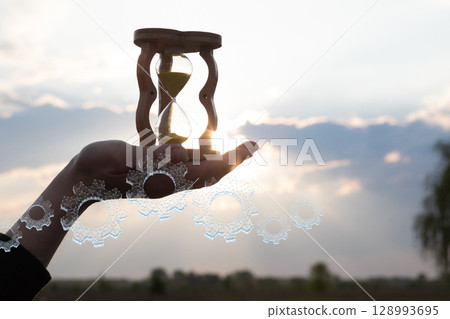 Holding time in an hourglass against sunset 128993695