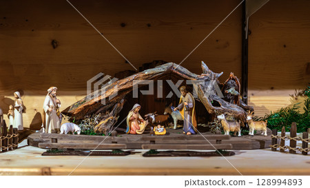 Christmas nativity scene with figurines. Traditional nativity scene, figurines of holy family, animals, wooden stable illuminated by warm light. Concept of nativity, Christian holiday symbolism Christmas nativity scene with figurines. Traditional nativity scene, figurines of holy family, animals, wooden stable illuminated by warm light. Concept of nativity, Christian holiday symbolism 128994893