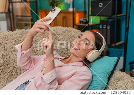 Young woman scrolling social media on smartphone with wireless headphones enjoying restful downtime Young woman scrolling social media on smartphone with wireless headphones enjoying restful downtime 128994923
