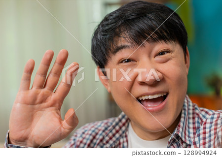 Asian man laughing gesturing during POV video call, lively friend conversation, joyful communication 128994924