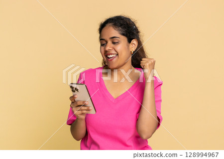 Indian woman happily looking smartphone screen, jumping joyfully, celebrating great online news 128994967