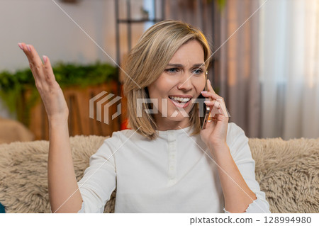 Adult woman arguing on smartphone at home, waving hands nervously with anger and expressive emotion 128994980