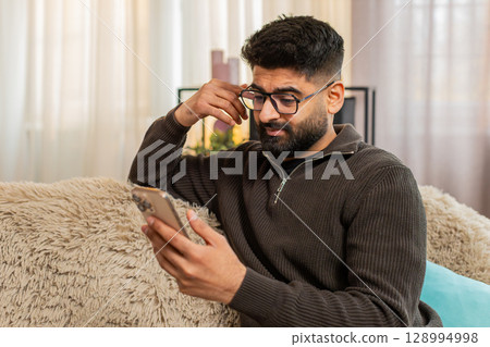 Indian man looking sadly at ex-girlfriend profile on smartphone, nostalgic emotional reaction Indian man looking sadly at ex-girlfriend profile on smartphone, nostalgic emotional reaction 128994998