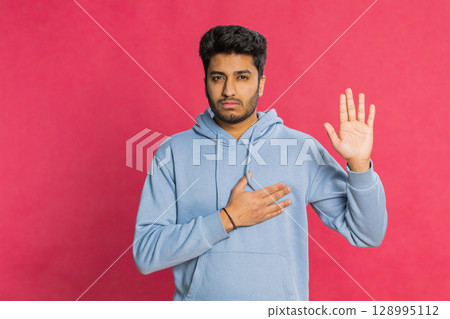 Indian man raising hand to take oath, promising to be honest and to tell truth keeping hand on chest 128995112