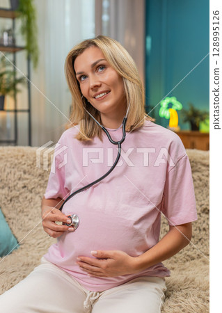 Pregnant woman using stethoscope on belly hearing baby moves showing focused gentle care attention Pregnant woman using stethoscope on belly hearing baby moves showing focused gentle care attention 128995126