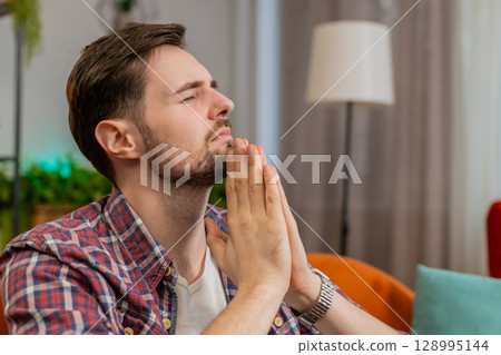 Tensed young man folding palms together pray to God ask for help feel stressed looks desperate 128995144