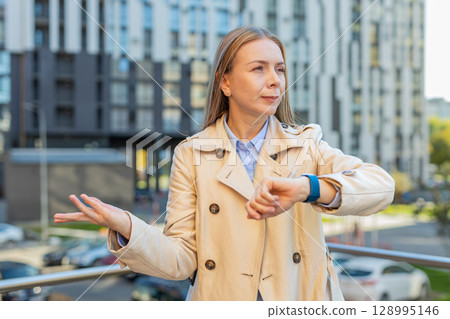 Serious sad mature businesswoman standing outdoors looking around waiting for business meeting Serious sad mature businesswoman standing outdoors looking around waiting for business meeting 128995146