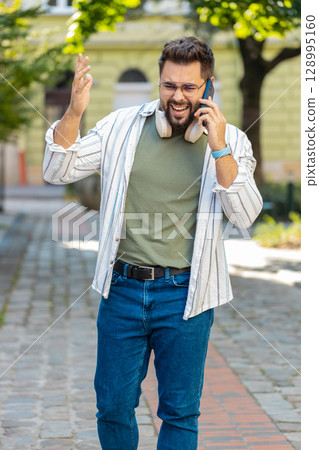 Caucasian young man traveler arguing talking on smartphone while walking on urban city street Caucasian young man traveler arguing talking on smartphone while walking on urban city street 128995160