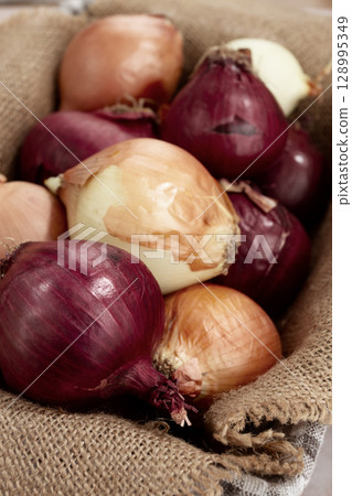 Various varieties of onions, in a basket, on a wooden surface, rustic style, close-up, no people 128995349