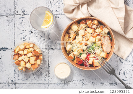 Caesar salad in a paper container, take it on the way, with sauce and croutons, on the table, snack, no people, 128995351