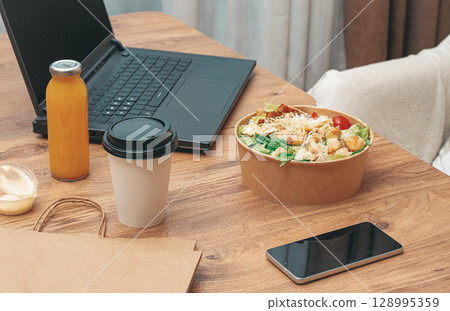 work at home on a laptop, there is food on the table, salad, coffee and juice, delivery, there are no people, 128995359