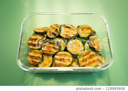 Fried zucchini slices on a glass bowl on a green background 128995608