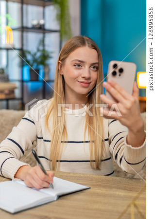 Woman talking on smartphone video call in serious business negotiation at home on sofa, making notes Woman talking on smartphone video call in serious business negotiation at home on sofa, making notes 128995858