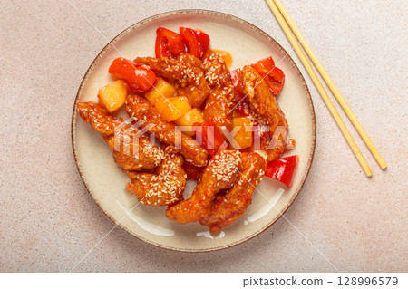 Asian sweet and sour chicken with pineapple and bell peppers on a plate with chopsticks top view 128996579