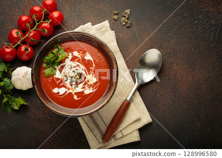 Tomato soup with cream, pumpkin seeds and herbs on brown background top view, copy space 128996580