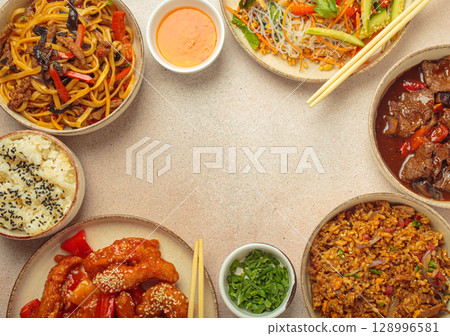 Variety of Chinese food dishes top view on table with chopsticks forming a frame with space for text, light beige background, cuisine of China 128996581