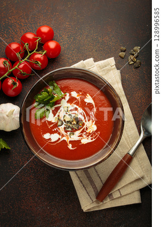 Tomato soup with cream, pumpkin seeds and herbs on brown background top view Tomato soup with cream, pumpkin seeds and herbs on brown background top view 128996585