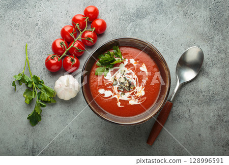 Tomato soup with cream, pumpkin seeds and herbs on grey background top view 128996591