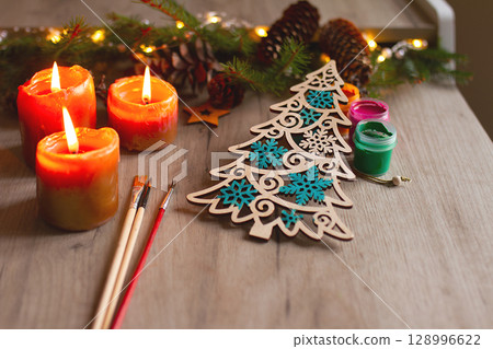 Winter painted wooden toy Christmas tree with brushes, paints, spruce branches, pinecones and candles on table 128996622