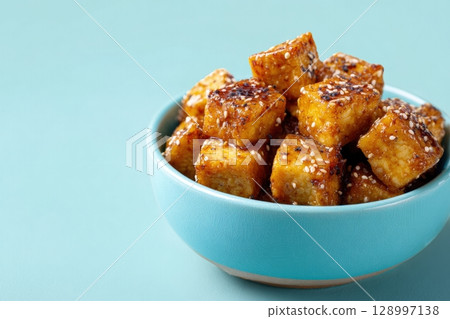Bowl of Baked Tofu Cubes with Sesame Glaze on Pastel Green Background Bowl of Baked Tofu Cubes with Sesame Glaze on Pastel Green Background 128997138
