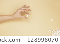 A white pill in a woman's hand on a beige background. The concept of first aid. 128998070