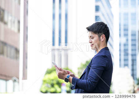 A young businessman operating a smartphone in an office district A young businessman operating a smartphone in an office district 128999476