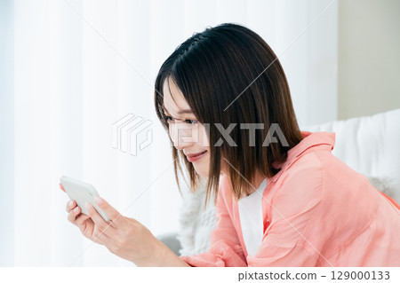 A young lady watching a smartphone on a sofa A young lady watching a smartphone on a sofa 129000133