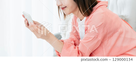 A young lady watching a smartphone on a sofa A young lady watching a smartphone on a sofa 129000134