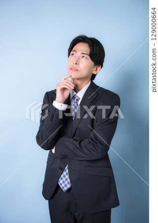 一位年輕商人穿著西裝，擺出思考和擔憂的姿態。淺藍色背景 129000664
