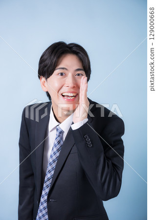 A male office worker posing in a secret pose for a private conversation. Refreshing light blue background. Image of job change, job recruitment, etc. Front vertical 129000668