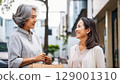 Two middle-aged women chatting on a street corner 129001310