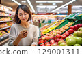 A woman looking at her smartphone while shopping at a supermarket 129001311