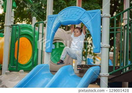 happy toddler girl hanging the red bar by her hand at outdoor playground in park happy toddler girl hanging the red bar by her hand at outdoor playground in park 129001428