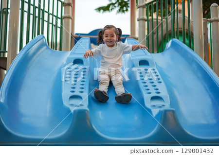 happy toddler baby girl sliding and playing at playground 129001432
