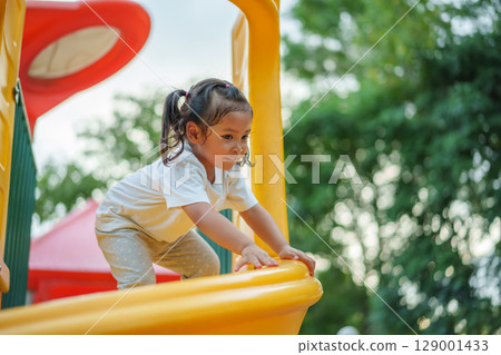 happy toddler baby girl sliding and playing at playground 129001433