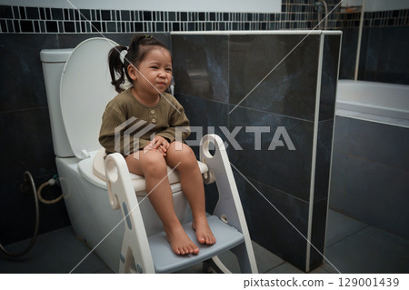 toddler girl sitting on toilet at home and suffering from stomachache and constipation toddler girl sitting on toilet at home and suffering from stomachache and constipation 129001439