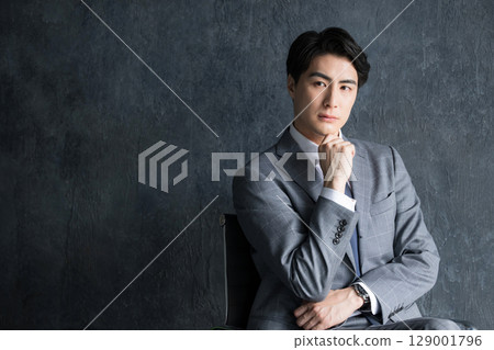 灰色背景中，一位穿著西裝的商人坐在椅子上的上半身 129001796