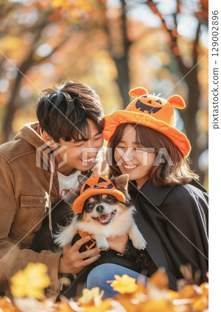 A smiling couple and their Shiba Inu relaxing among the autumn leaves 129002896