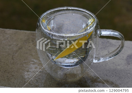 Glass Mug with Water and Yellow Leaf on Rainy Day  129004795