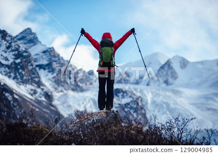 Backpacking woman hiking face a large hanging glacier on high altitude mountain top 129004985