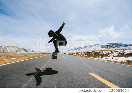 Skateboarder skateboarding on snowy country road Skateboarder skateboarding on snowy country road 129005004
