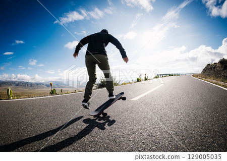 Skateboarder skateboarding on the mountain road 129005035