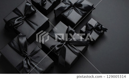 Wrapped in a red ribbon and bow, a festive black gift box sits isolated on a dark background, perfect for a surprise birthday or holiday present 129005314