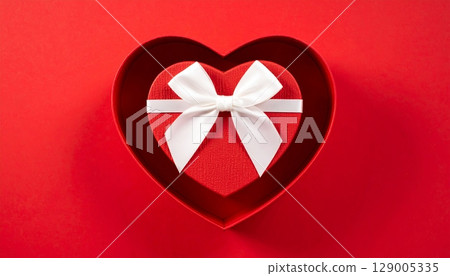 Red gift box with a ribbon and a bow on a heart-shaped design for a celebration of love, birthday, or holiday surprise Red gift box with a ribbon and a bow on a heart-shaped design for a celebration of love, birthday, or holiday surprise 129005335
