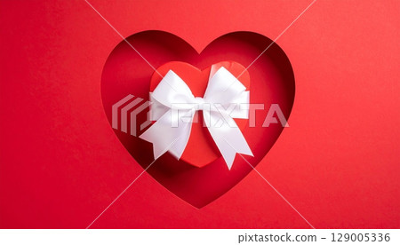 Red gift box with a ribbon and a bow on a heart-shaped design for a celebration of love, birthday, or holiday surprise Red gift box with a ribbon and a bow on a heart-shaped design for a celebration of love, birthday, or holiday surprise 129005336